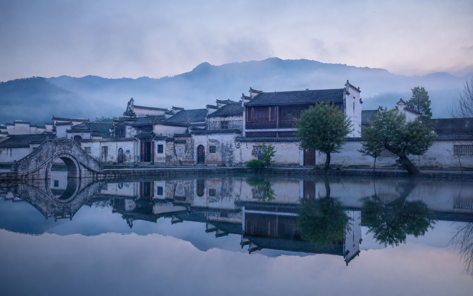 Hongcun at dawn with still water, white walls, and mist-softened rooftops